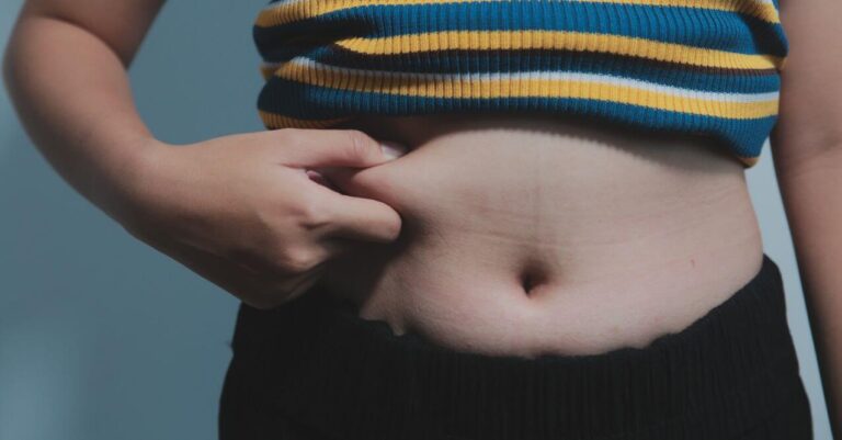 A person pinching their belly fat, resembling 'How to Get Your Body to Burn Stored Fat'.