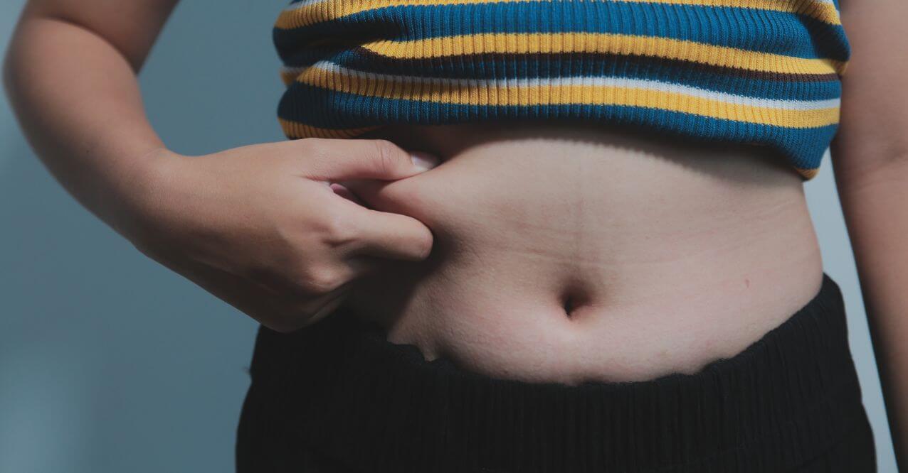 A person pinching their belly fat, resembling 'How to Get Your Body to Burn Stored Fat'.