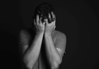 Black and white image of a man holding his head due to nervousness, covering hhead with hands