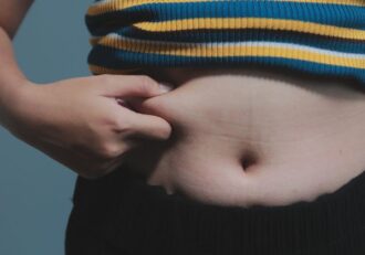 A person pinching their belly fat, resembling 'How to Get Your Body to Burn Stored Fat'.